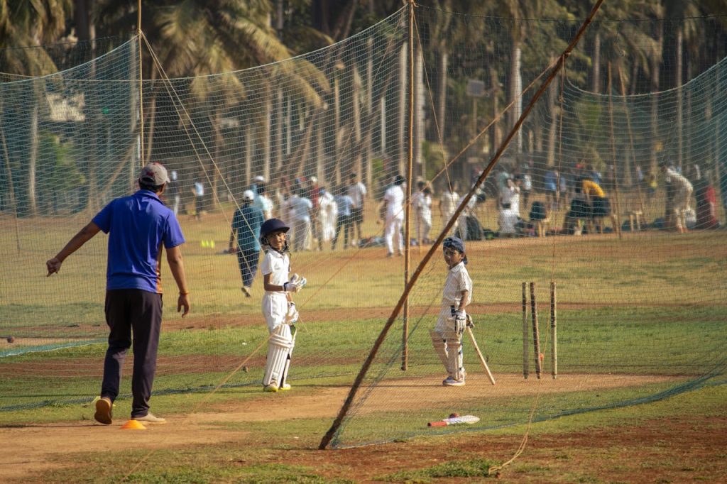 Young boys practicing cricket with coach in a Mumbai park. Sunny day, outdoor sports scene.